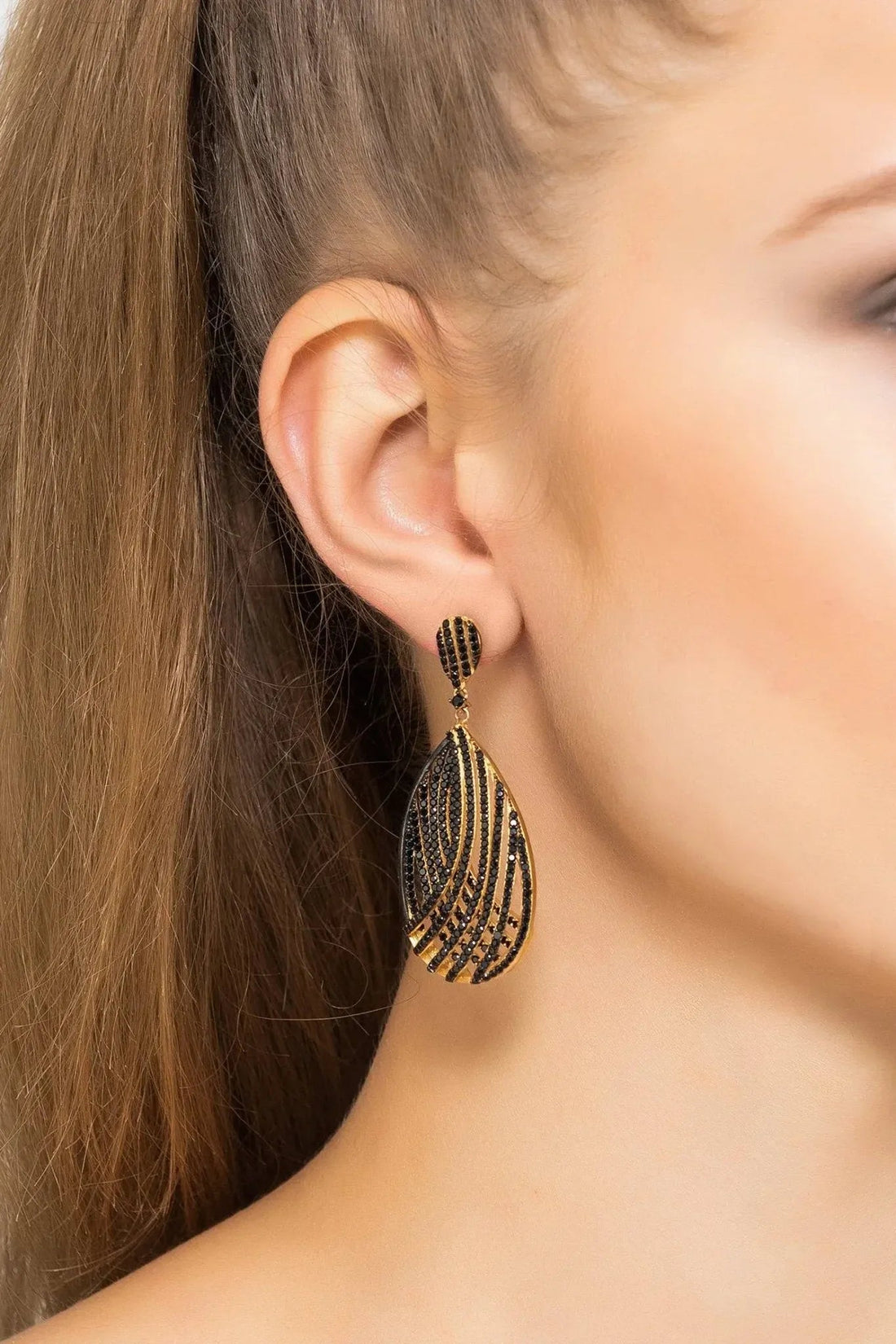 Black CZ teardrop earrings with gold-toned lattice detail, worn on the ear