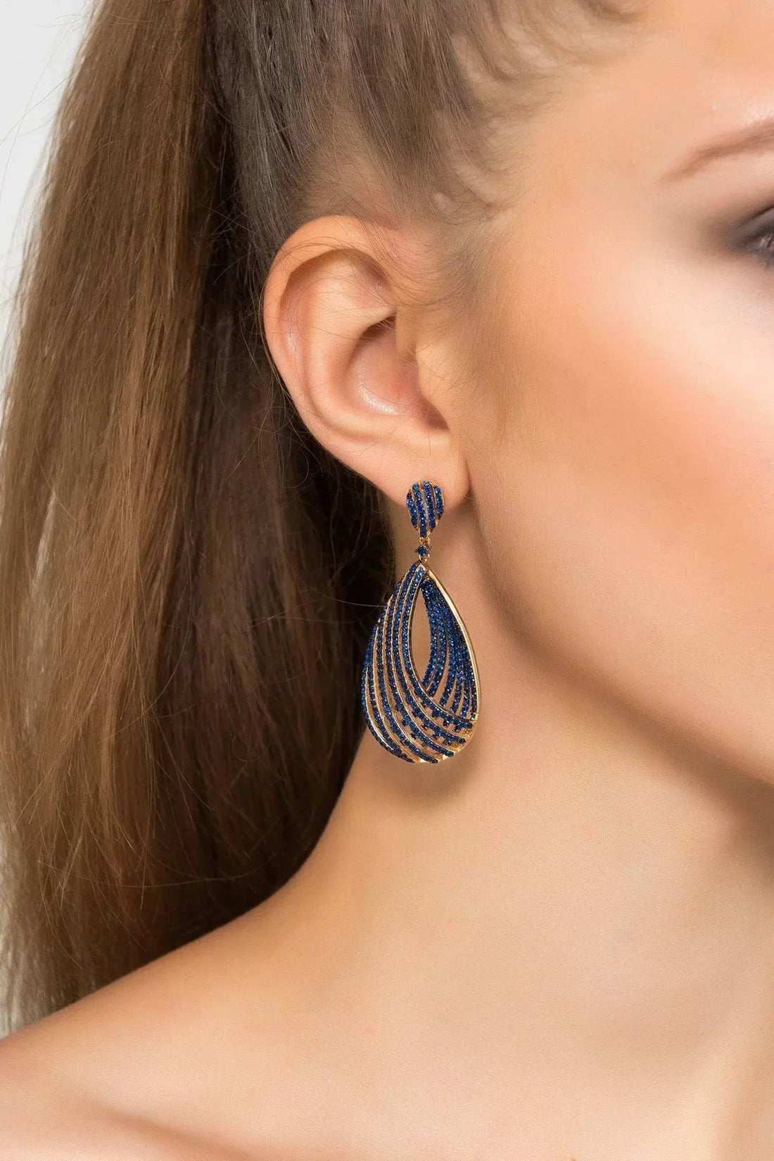 Gold-tone sapphire blue CZ teardrop hoop earrings worn on ear