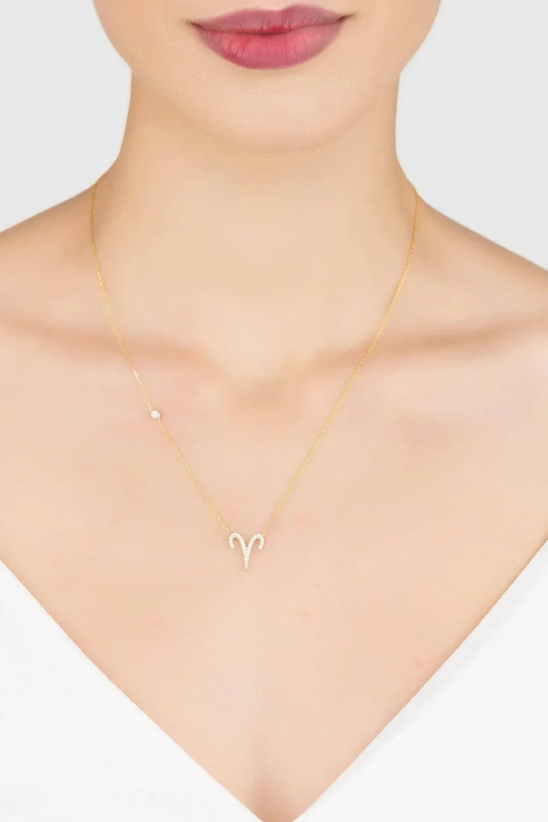 Gold Aries zodiac pendant necklace on model neckline, small rhinestone charm