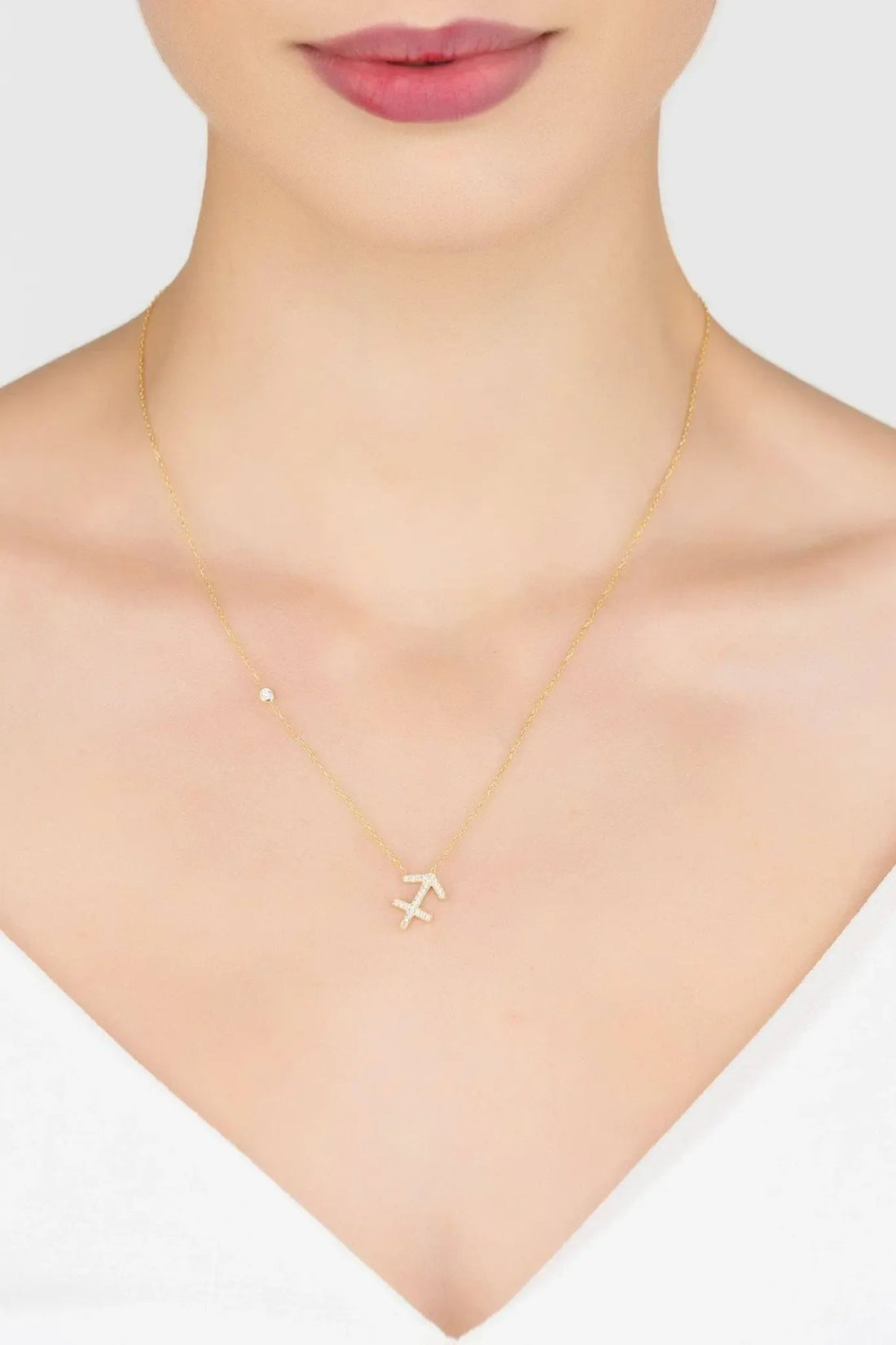 Gold Sagittarius pendant necklace with stylized symbol charm worn on neckline